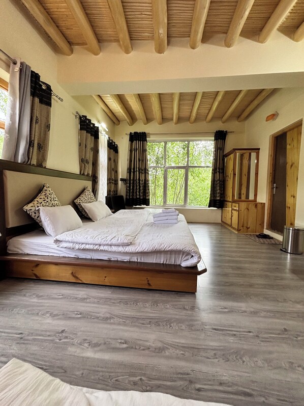 A bedroom with a wooden bed, large windows, and a view of greenery.