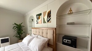 Un lit bien fait, avec du linge de lit blanc, une tête de lit et une petite table de chevet sur laquelle se trouve une radio.