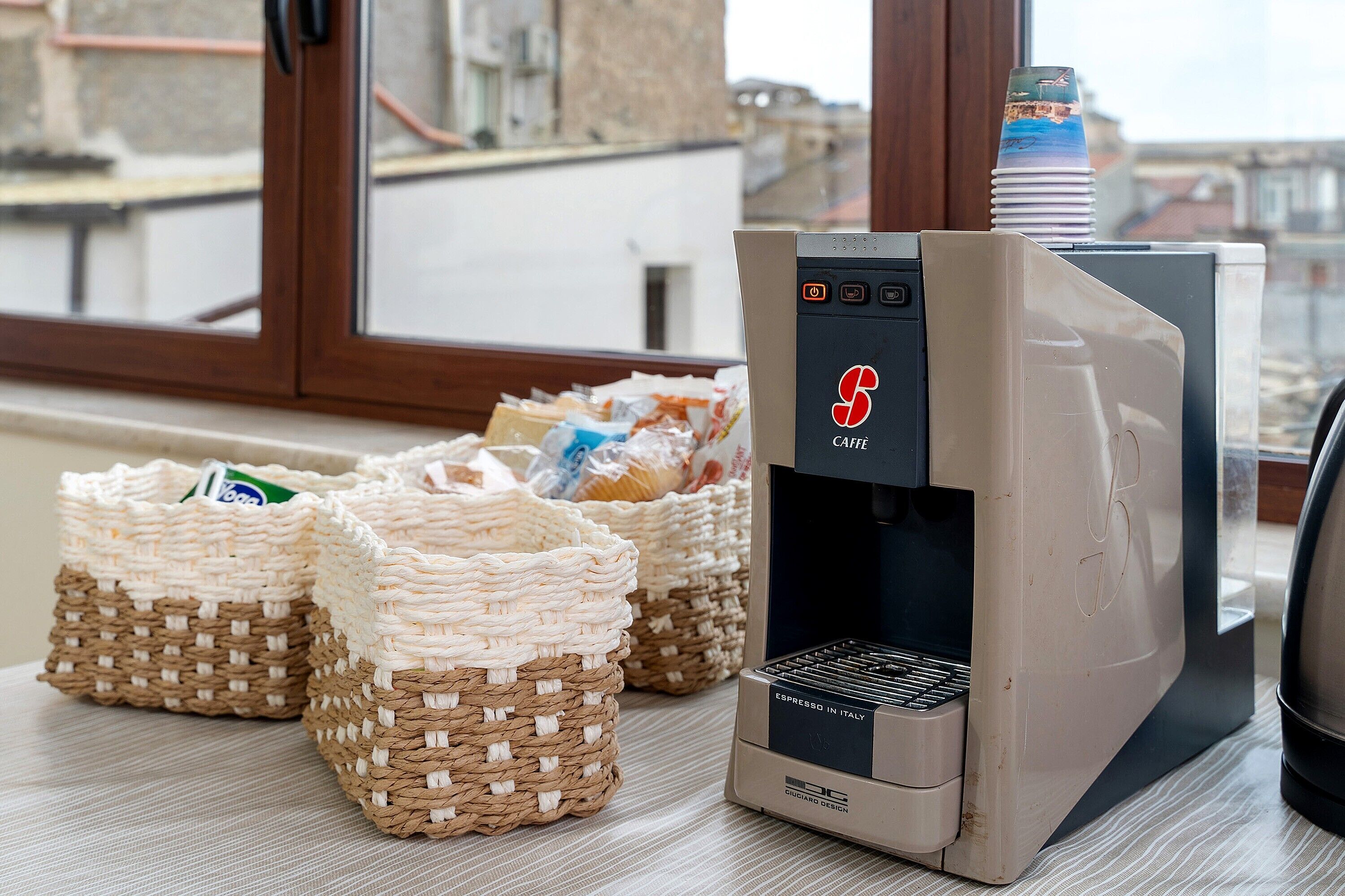 A coffee machine with baskets of coffee pods, a window with a view of buildings, and a door.