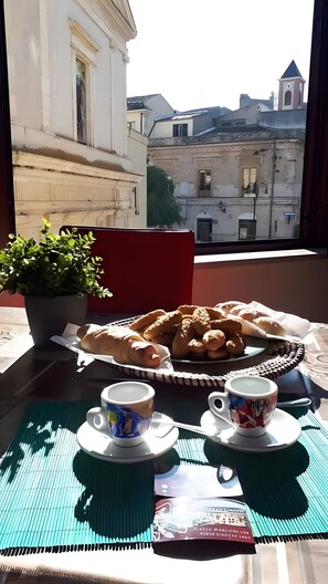 Ein Tisch mit Gebäck, zwei Tassen und einem Blumentopf vor einem Fenster mit Blick auf Gebäude.