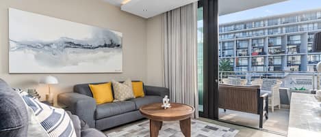 A modern living room with a grey sofa, a round wooden coffee table, and a large abstract painting on the wall.