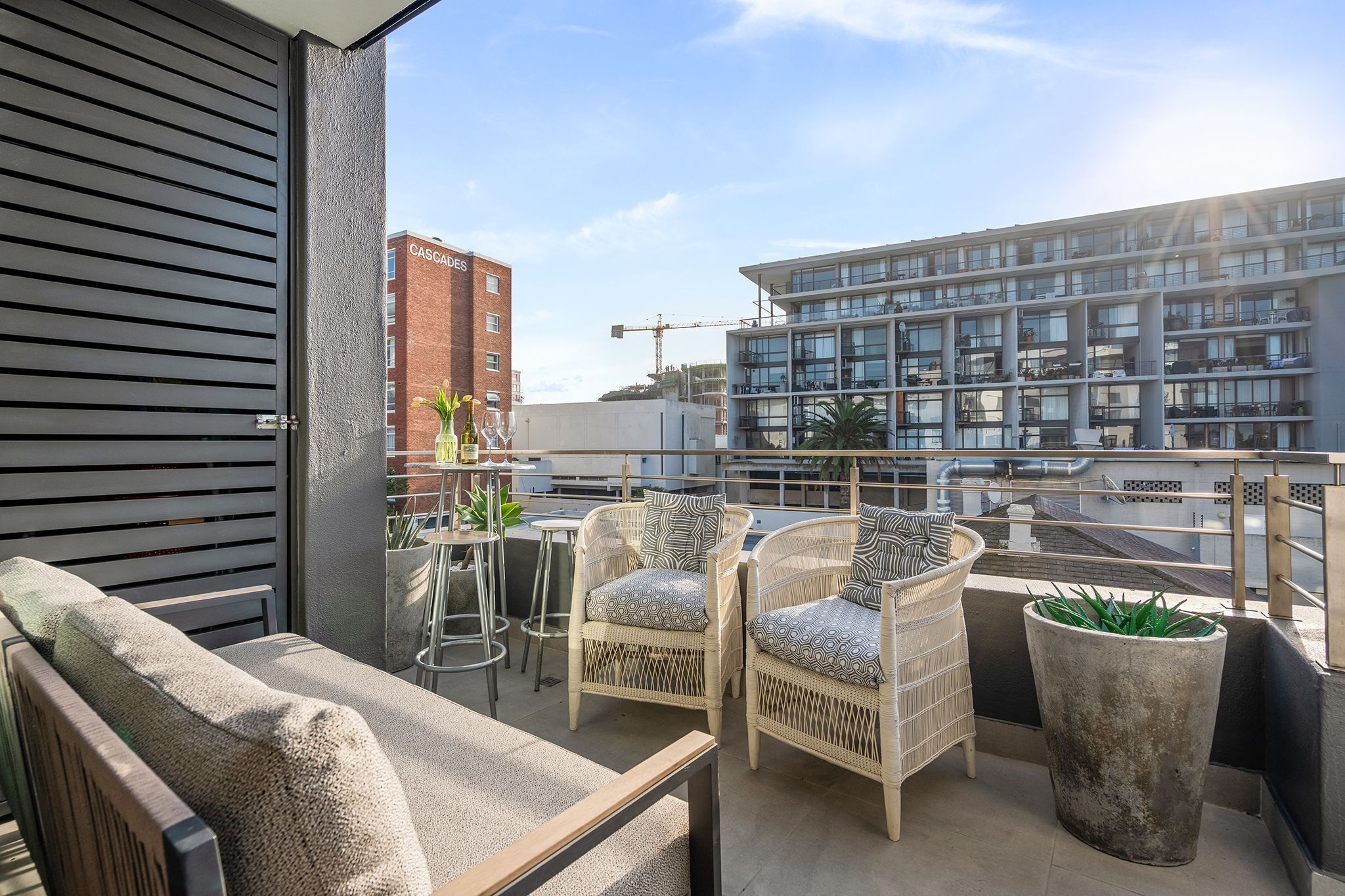 A balcony with wicker chairs, a potted plant, and a view of a modern building.