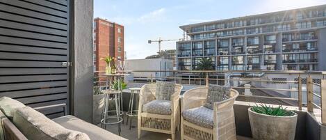 A balcony with wicker chairs, a potted plant, and a view of a modern building.