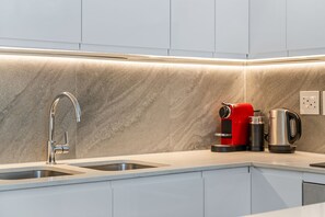 Eine moderne Küche mit einem Edelstahl-Spülbecken, einer roten Kaffeemaschine und einem Wasserkocher auf der Arbeitsplatte.