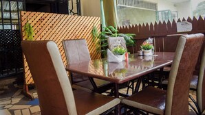 Un restaurante con un separador de madera, sillas con cojines, una mesa de vidrio y plantas en macetas.
