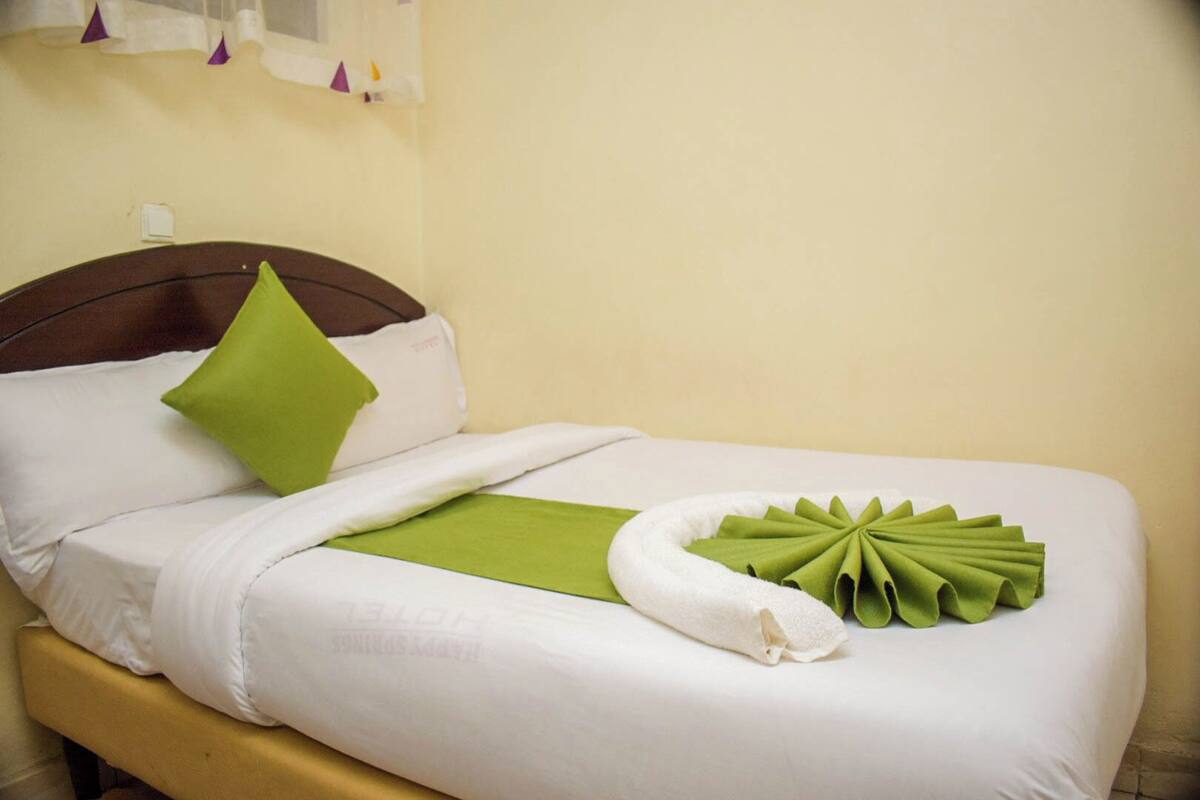 A neatly made bed with white linens, a green pillow, and a towel arranged on the bed.