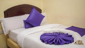 Una cama bien hecha con sábanas blancas, una almohada morada y un adorno morado sobre la cama.