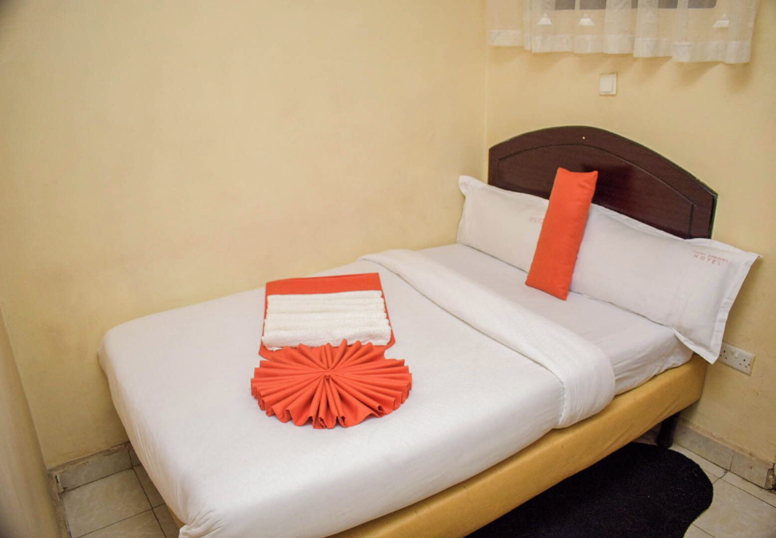 A bed with white bedding, a brown headboard, and a red and white decorative item on the bed.