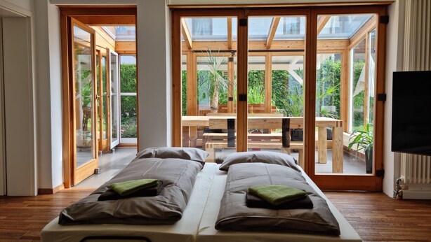 A modern room with a bed, a TV, and large windows.