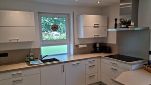 A modern kitchen with white cabinets, a sink, a stove, and a window with a view of greenery.