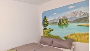 A bedroom with a bed, pillows, and a wall mural of a lake and mountains.