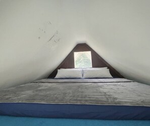 Ein kleines, dreieckiges Schlafzimmer im Dachgeschoss mit einem Einzelbett, einem Fenster und einer geneigten Decke.