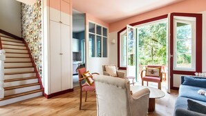 Una escala condueix a una habitació amb vistes a vegetació, una zona de menjador amb taula i cadires, i un sofà.