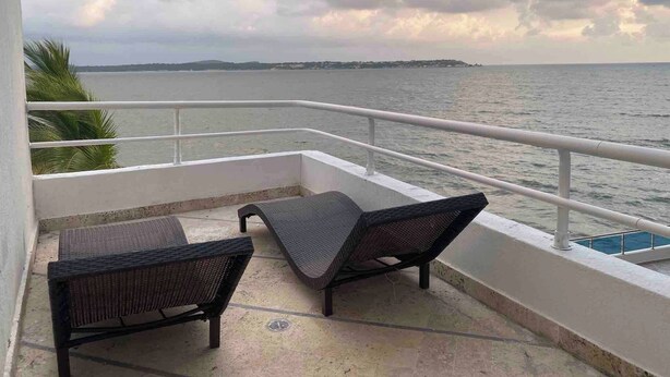 A balcony with two wicker chairs, a pool, and a view of the sea and distant land. - 1 Bedroom Private Jacuzzi and Direct Beach Access (Cartagena)
