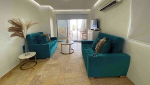 A modern living room with teal sofas, a small round table, and a large window. - 1 Bedroom Private Jacuzzi and Direct Beach Access (Cartagena)