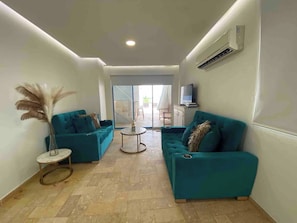 Ein modernes Wohnzimmer mit türkisfarbenen Sofas, einem kleinen runden Tisch und einem großen Fenster.
