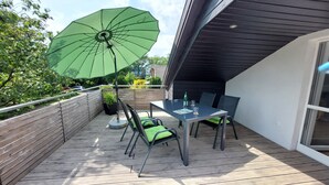 Une terrasse avec une table et des chaises, un parasol vert et une vue sur les environs.