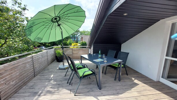 A deck with a table and chairs, a green umbrella, and a view of the surrounding area. - Apartment Abel with Balcony, Wi-Fi, Charging Station & AC near Hospital and Rehab Center (Oldenburg)