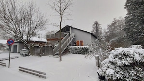 Un immeuble résidentiel avec un escalier menant au deuxième étage, une entrée fermée par un portail et un paysage enneigé.