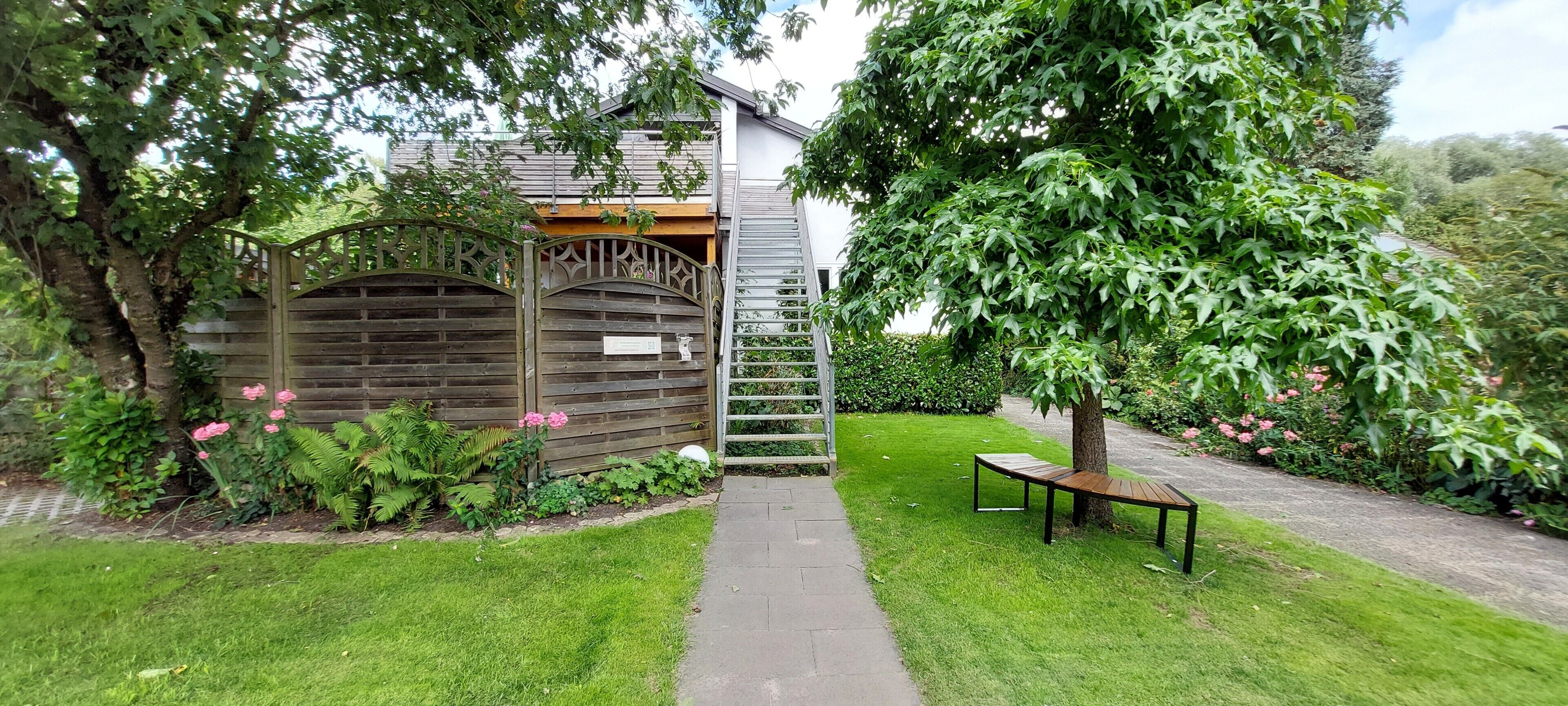 Ein Gartenweg führt zu einer Holzhütte mit einer Metalltreppe.