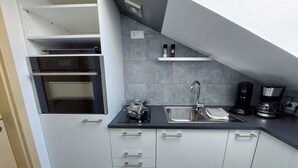 A modern kitchen with a built-in oven, a sink, and a coffee maker. - Apartment Abel with Balcony, Wi-Fi, Charging Station & AC near Hospital and Rehab Center (Oldenburg)