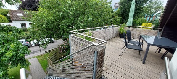 A wooden deck with a metal railing, a table, and chairs.