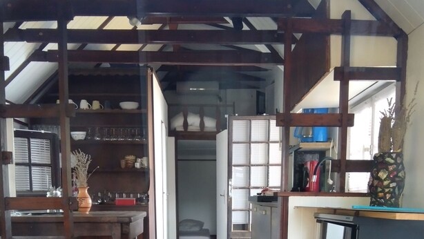 A narrow hallway with a wooden ceiling, a kitchen area with cabinets and a refrigerator, and a dining area with chairs and a table.