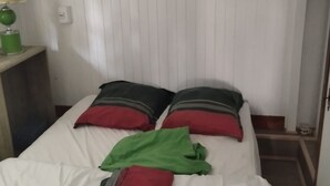 A single bed with white bedding, two pillows with red and grey stripes, and a green towel.