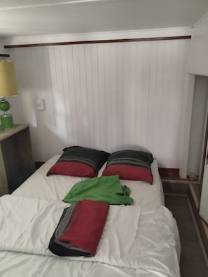 A single bed with white bedding, two pillows with red and grey stripes, and a green towel. - Beachfront cottage (Neuvic)