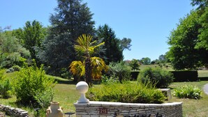A stone wall with a number sign, a palm tree, and various plants. - O Reflection of the Lake (Groléjac)