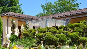 A traditional building with a tiled roof, surrounded by well-maintained shrubbery and a clear sky. - O Reflection of the Lake (Groléjac)