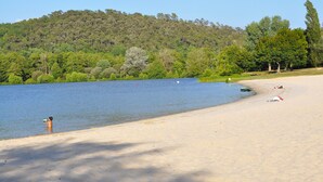 A beach with a sandy shore, a person in the water, and a boat on the sand. - O Reflection of the Lake (Groléjac)