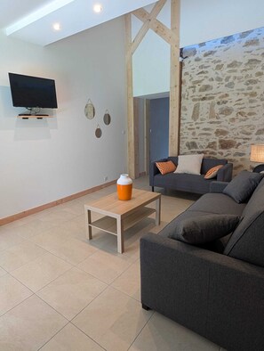A modern living room with a flat-screen TV, a wooden coffee table, a grey sofa, and a stone wall.