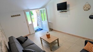 Een moderne woonkamer met een bank, salontafel, een aan de muur bevestigde televisie en een schuifdeur die leidt naar een buitenruimte.