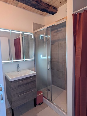 A modern bathroom with a glass shower enclosure, a vanity with a mirror, and a red curtain. - Gîte du Bosquet (Oradour-sur-Glane)