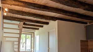 Een kamer met een houten plafond, een trap, een eettafel met stoelen en een raam.