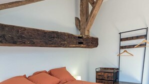 Een slaapkamer met een groot bed, houten balken, een nachtkastje en een kledingkast met ophanghaakjes.