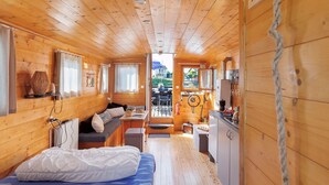 A wooden cabin interior with a bed, seating area, kitchenette, and a view through a door.