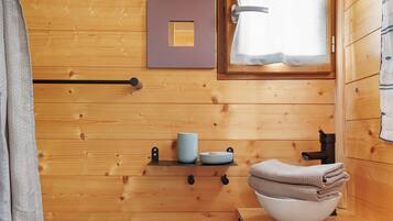 Ein Holzhütten-Innenraum mit einer Holzwand, einem Fenster mit Vorhang, einem Regal mit Tasse, Schüsseln und Handtüchern.