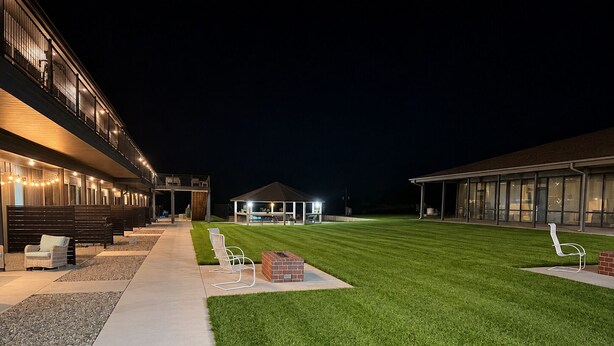 A well-lit outdoor area with a lawn, seating arrangements, and a building with large windows.