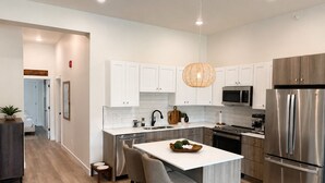 A modern kitchen with white cabinetry, stainless steel appliances, and a central island with bar stools.