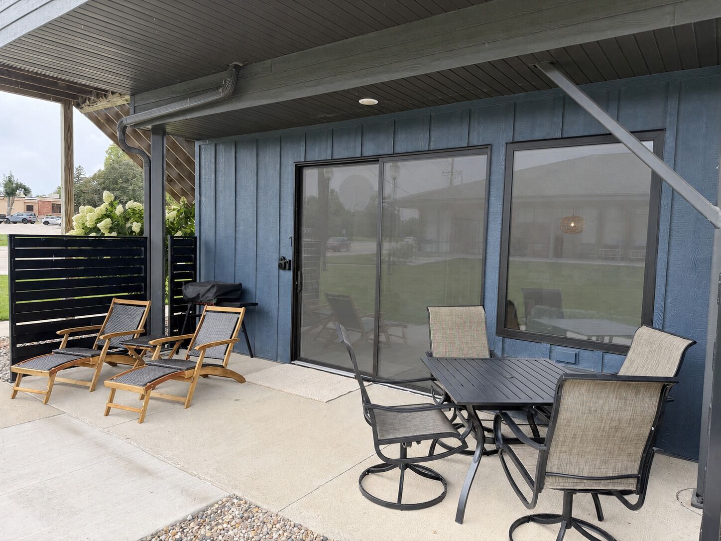 An outdoor patio with a table and chairs, a grill, and a covered area with a view of the backyard.