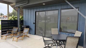 An outdoor patio with a table and chairs, a grill, and a covered area with a view of the backyard.