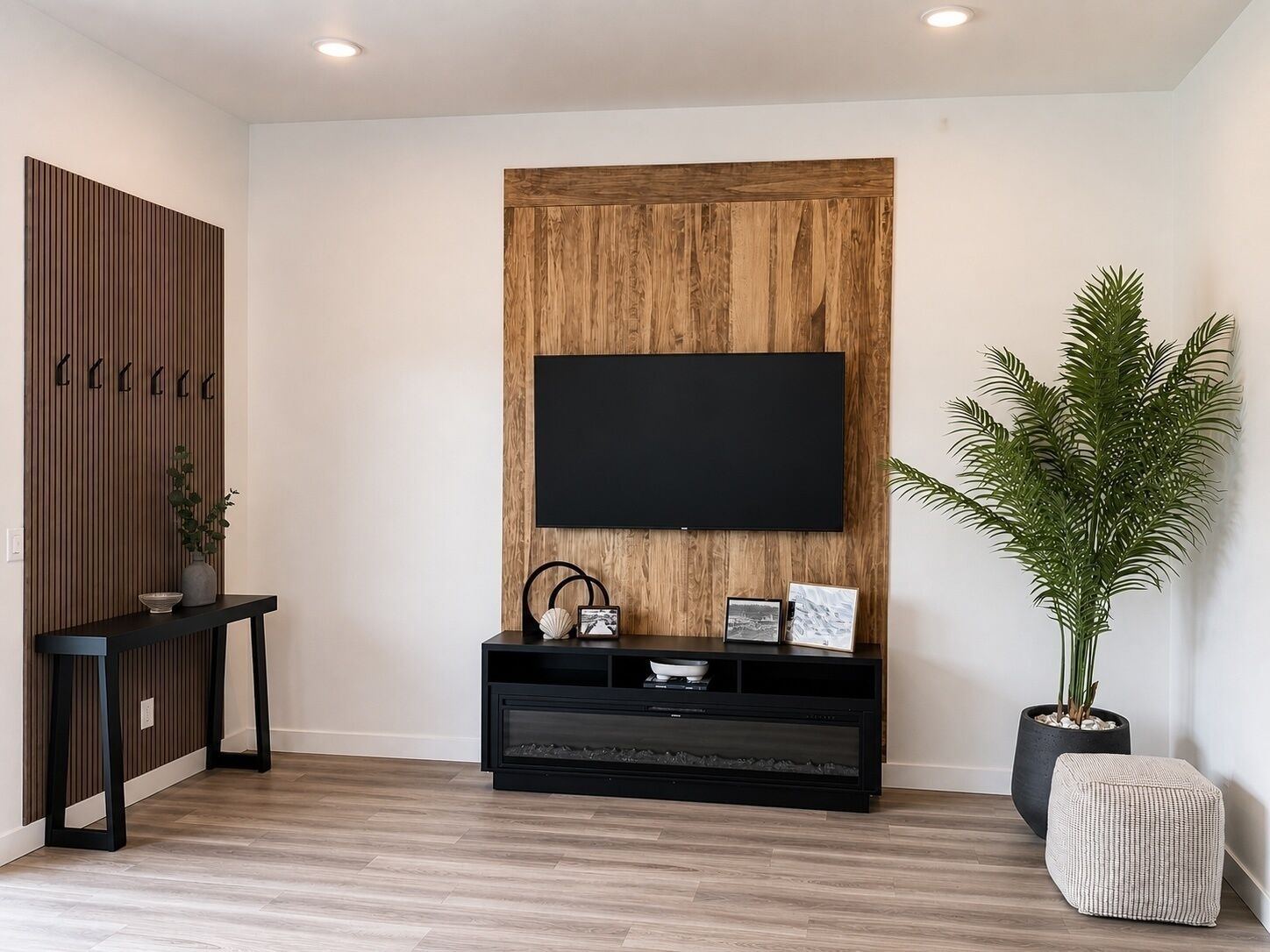 Una sala de estar moderna con un televisor de pantalla plana montado en una pared de madera, un mueble de entretenimiento negro debajo y una planta en maceta a la derecha.