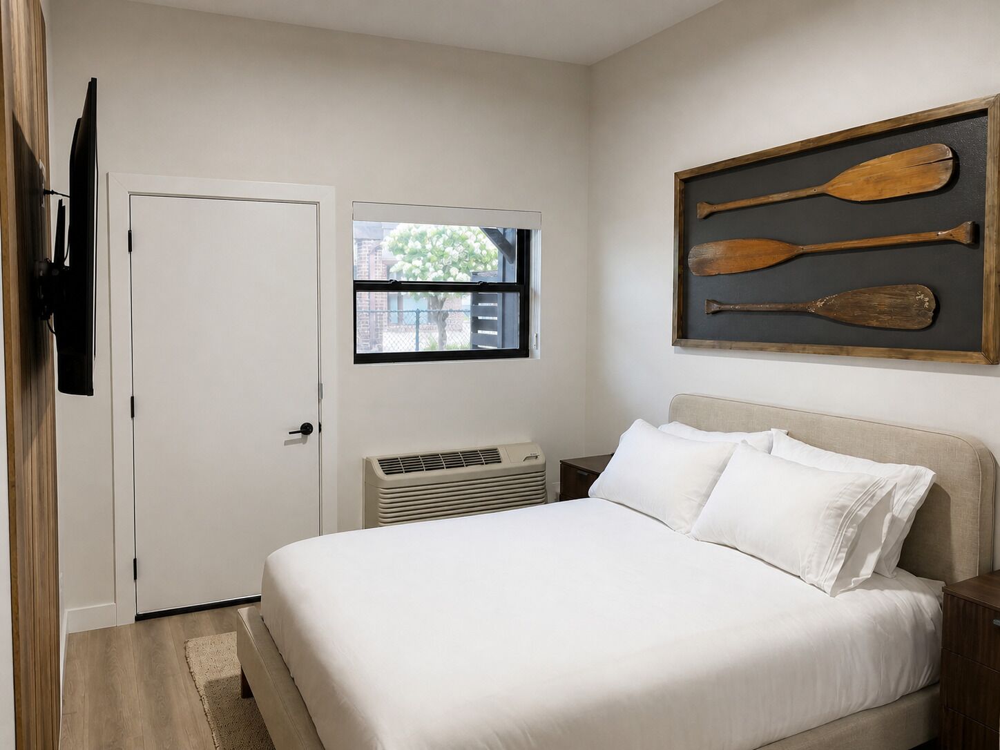 A bedroom with a bed, a window, a wall-mounted television, and a framed picture of paddles.