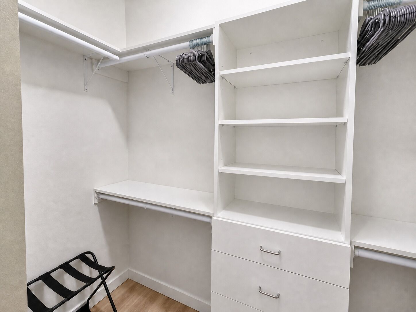 Un vestidor con estantes abiertos, barra para colgar y una silla negra.