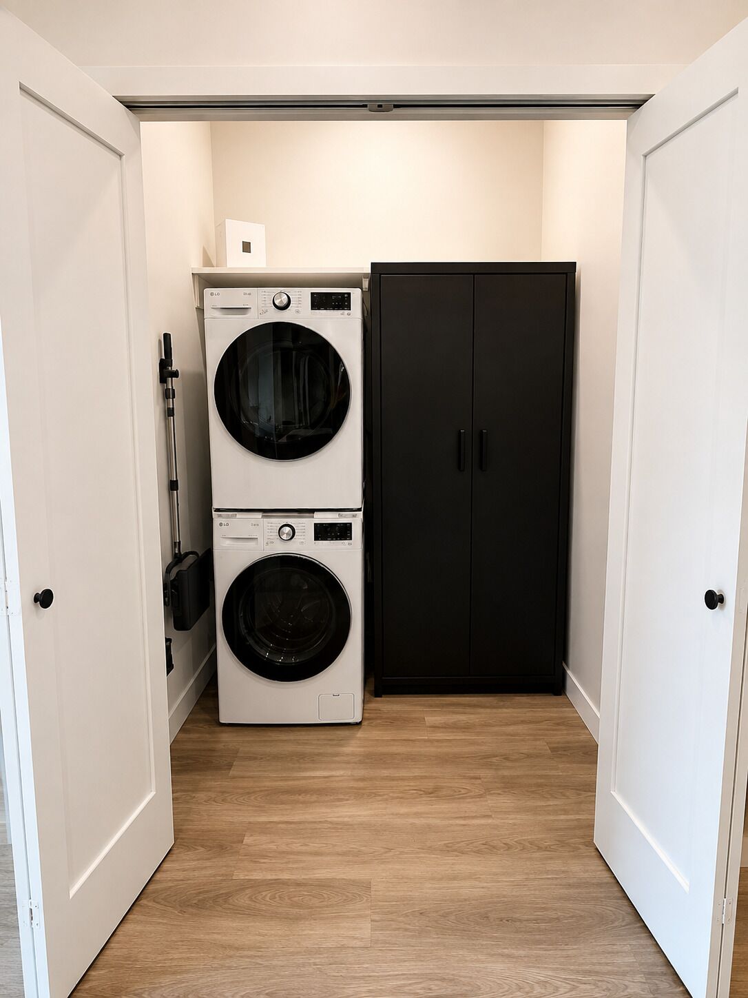 A laundry room with two stacked washing machines and a black cabinet.
