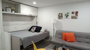 Ein gemütlicher Wohnraum mit Bett, Sofa, kleinem Tisch mit Lampe und zwei Stühlen.