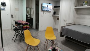 Ein Schlafzimmer mit einem Bett, einem Fernseher, einem Schreibtisch mit Stuhl und einem kleinen Tisch mit Zeitschriften.