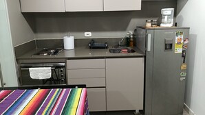 Eine kleine Küche mit Herd, Spüle und Kühlschrank, ausgestattet mit einer gestreiften Tischdecke und einer Kaffeemaschine.